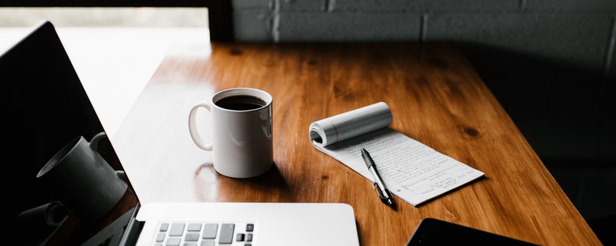 MacBook Pro, white ceramic mug,and black smartphone on table