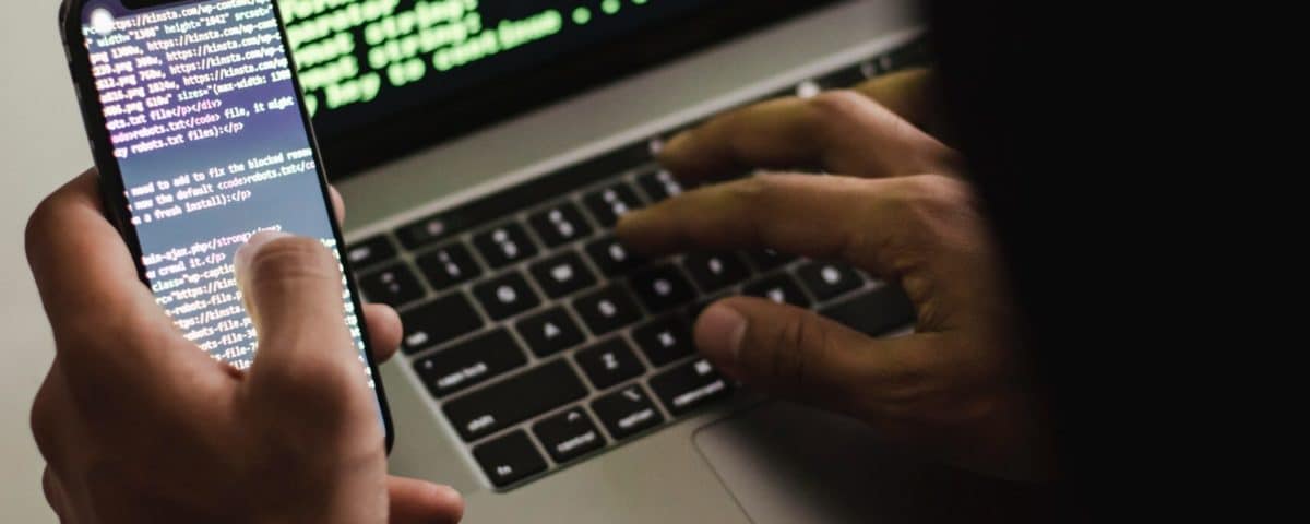 Free Unrecognizable hacker with smartphone typing on laptop at desk Stock Photo